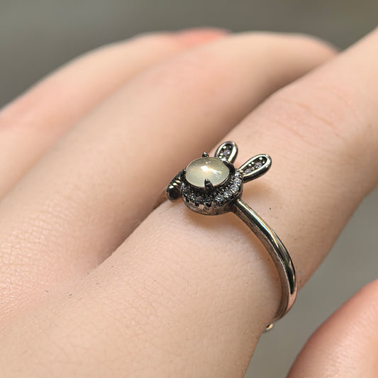 Angled view of a white jadeite rabbit ring worn on a finger, showing the round cabochon, clear accent halo and S925 silver rabbit ears.
