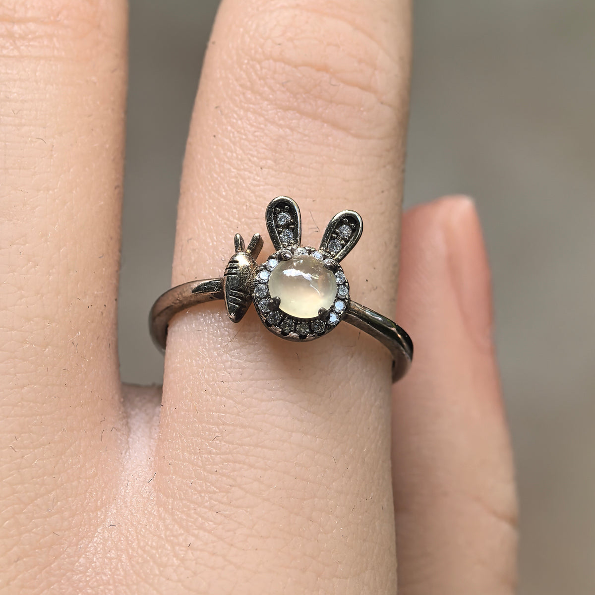 Front view of the white jadeite rabbit ring on a finger, with upright silver ears, clear accent stones and a small carrot motif.