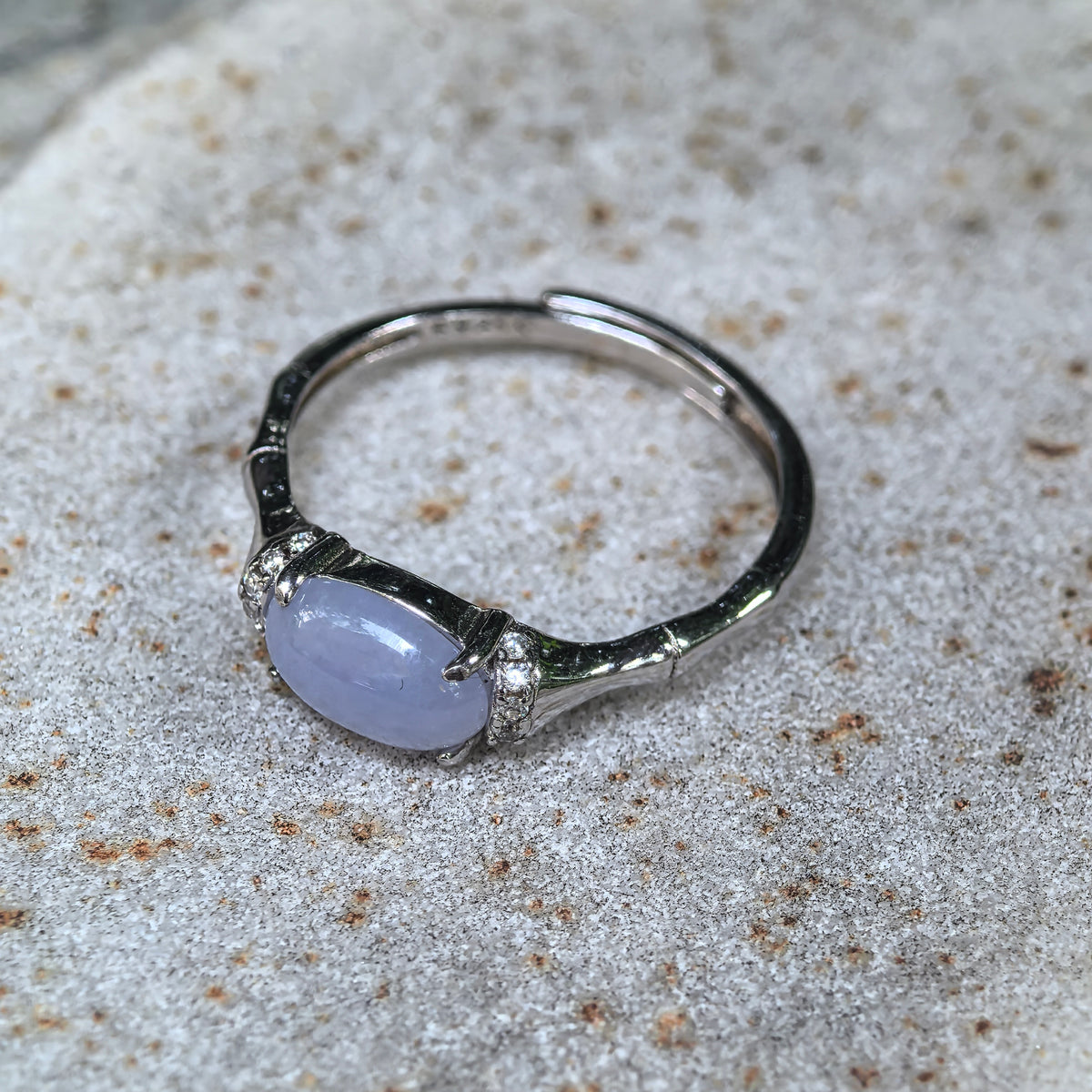 Angled view of a purple jadeite ring on stone, highlighting the tapered silver shoulders, segmented band details and adjustable opening.