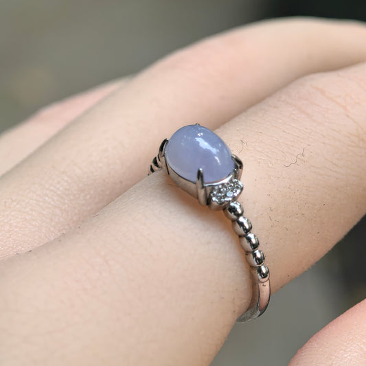Angled close-up of a purple oval jadeite ring worn on the finger, showing its S925 silver prongs, clear side accents and beaded shoulder details.