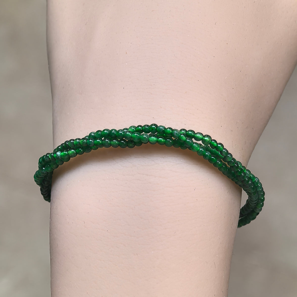 Front view of a twisted green jadeite bead bracelet on the wrist, showing its slender profile and polished beads.