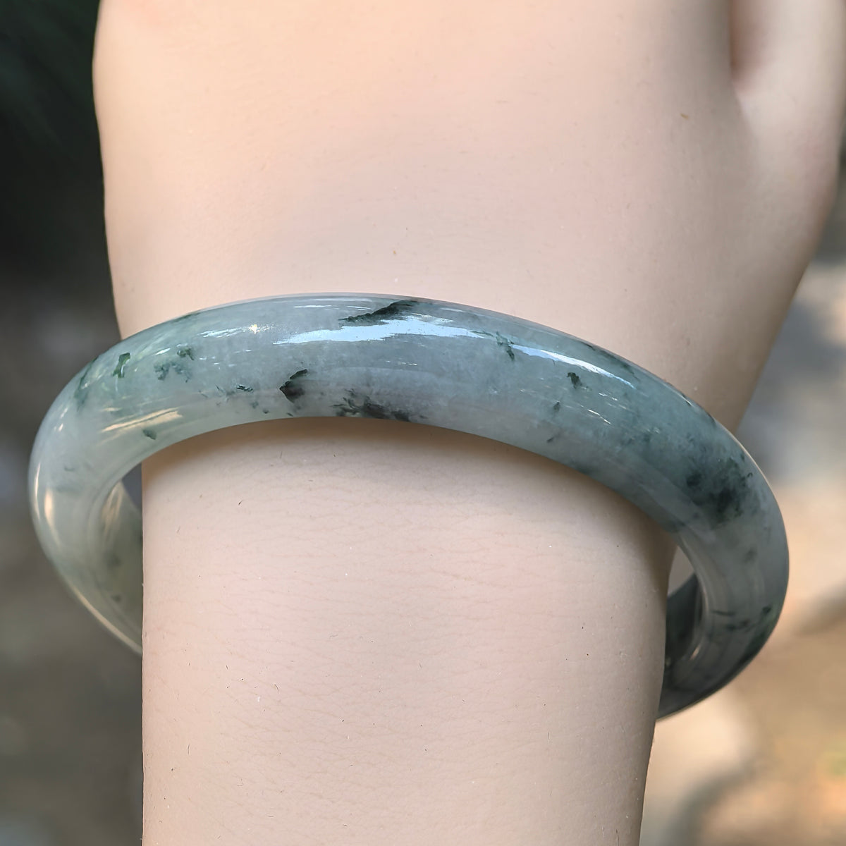 Front wrist view of a jadeite D-shape bangle with dark green floating patterns across a softly translucent white base.