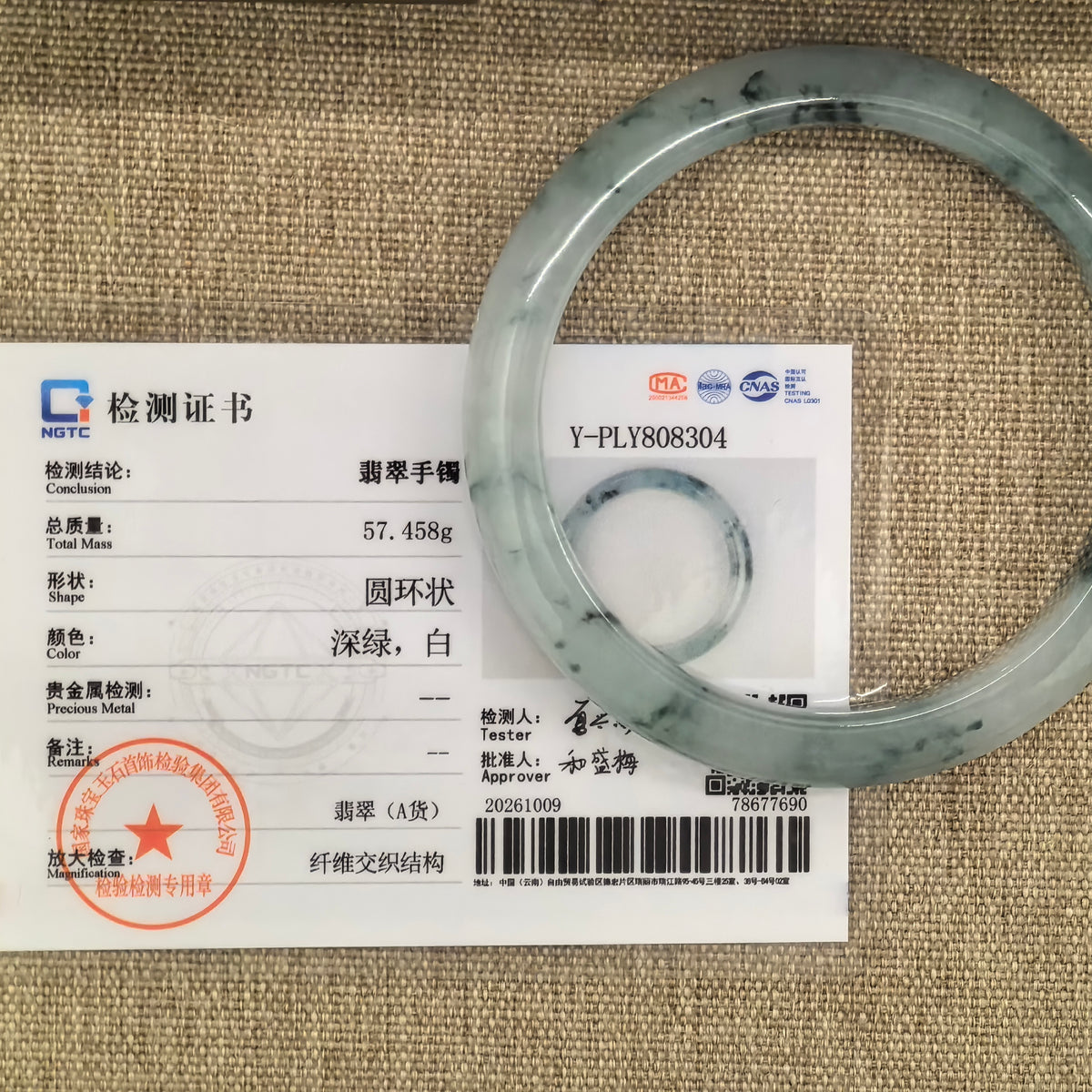 Jadeite bangle with dark green floating patterns displayed over its matching NGTC certificate on a woven background.