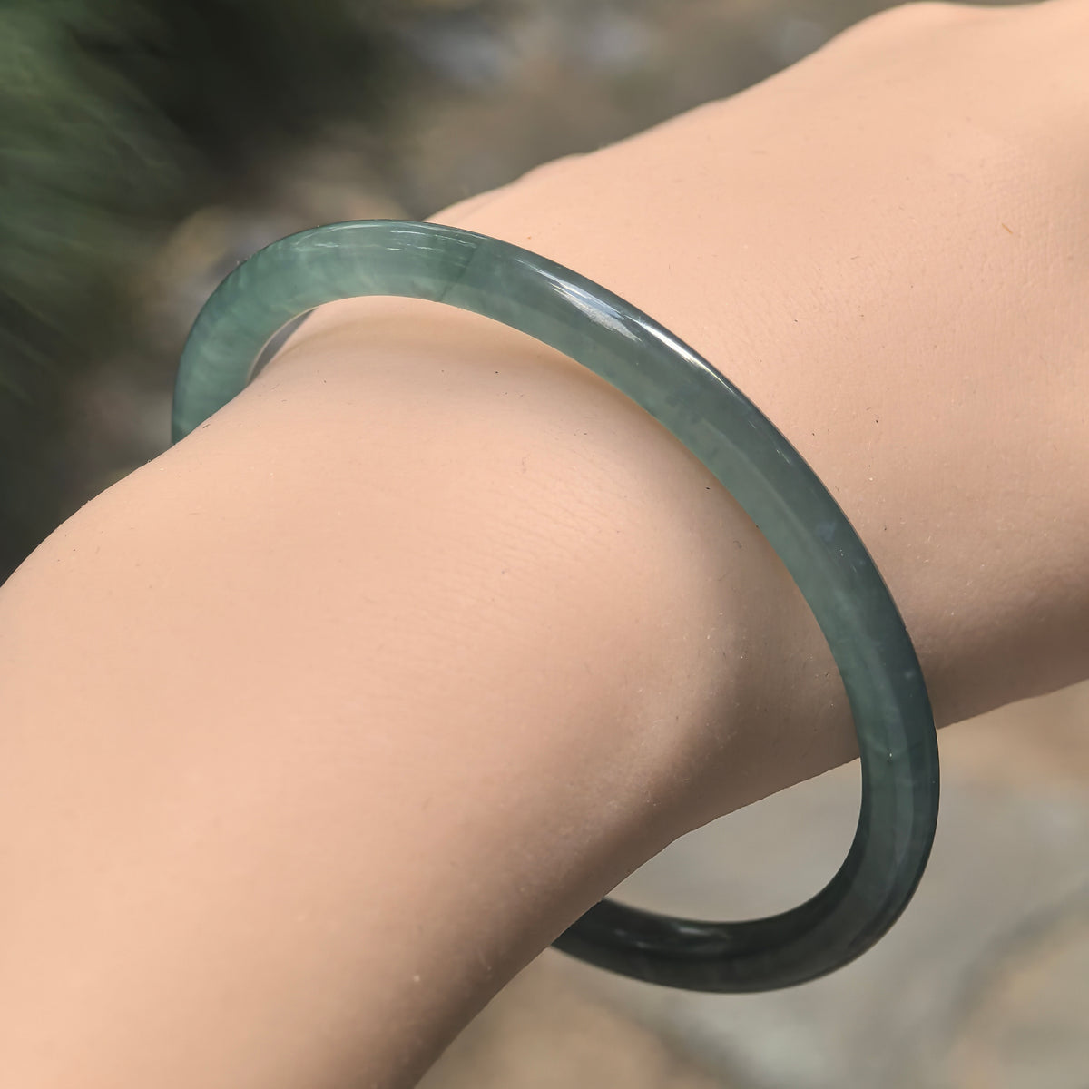 Angled wrist view of a slim green Guatemalan jadeite bangle, showing its rounded profile and polished surface.