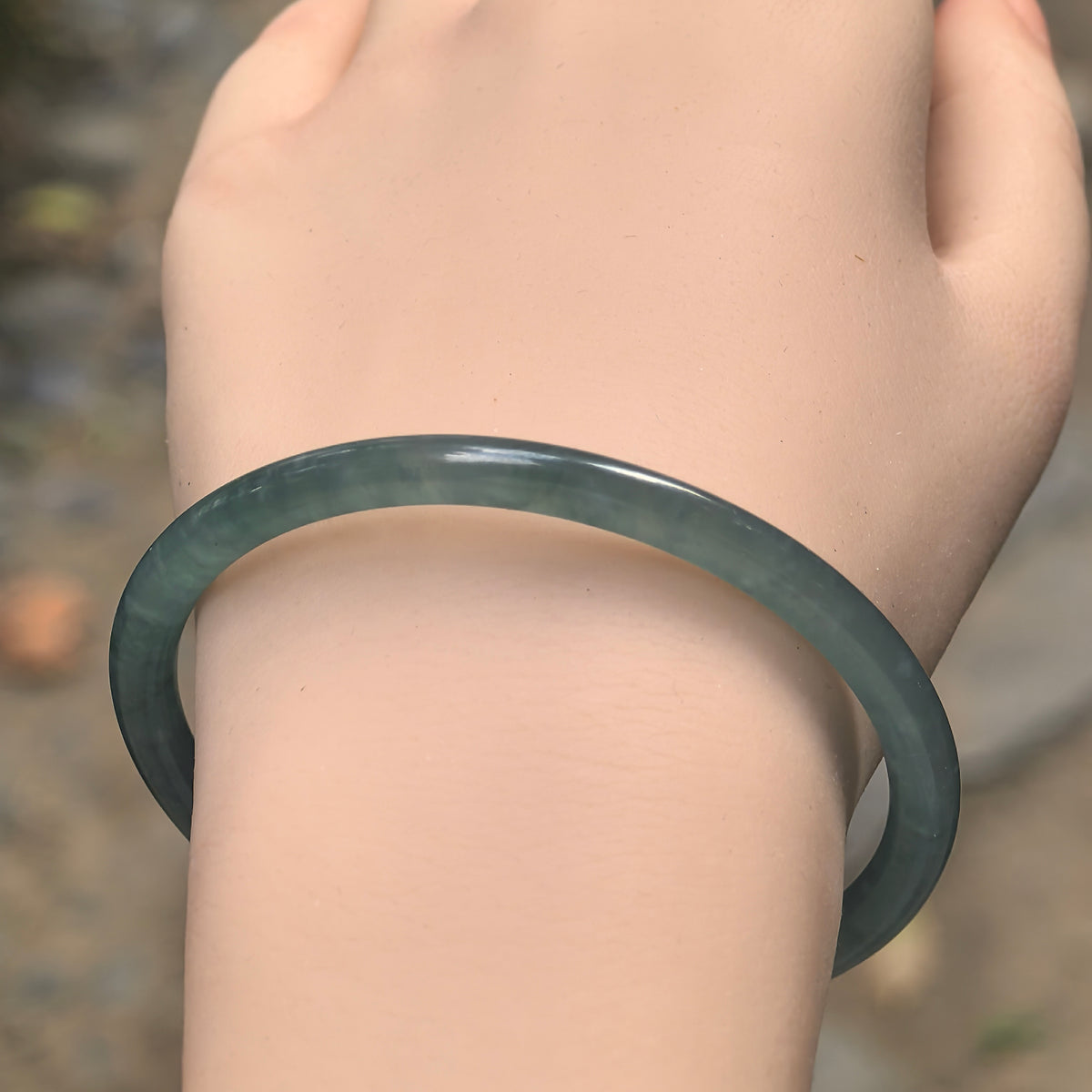 Green icy glutinous jadeite bangle worn on a wrist, with a slender round-bar shape and visible cotton-like inclusions.