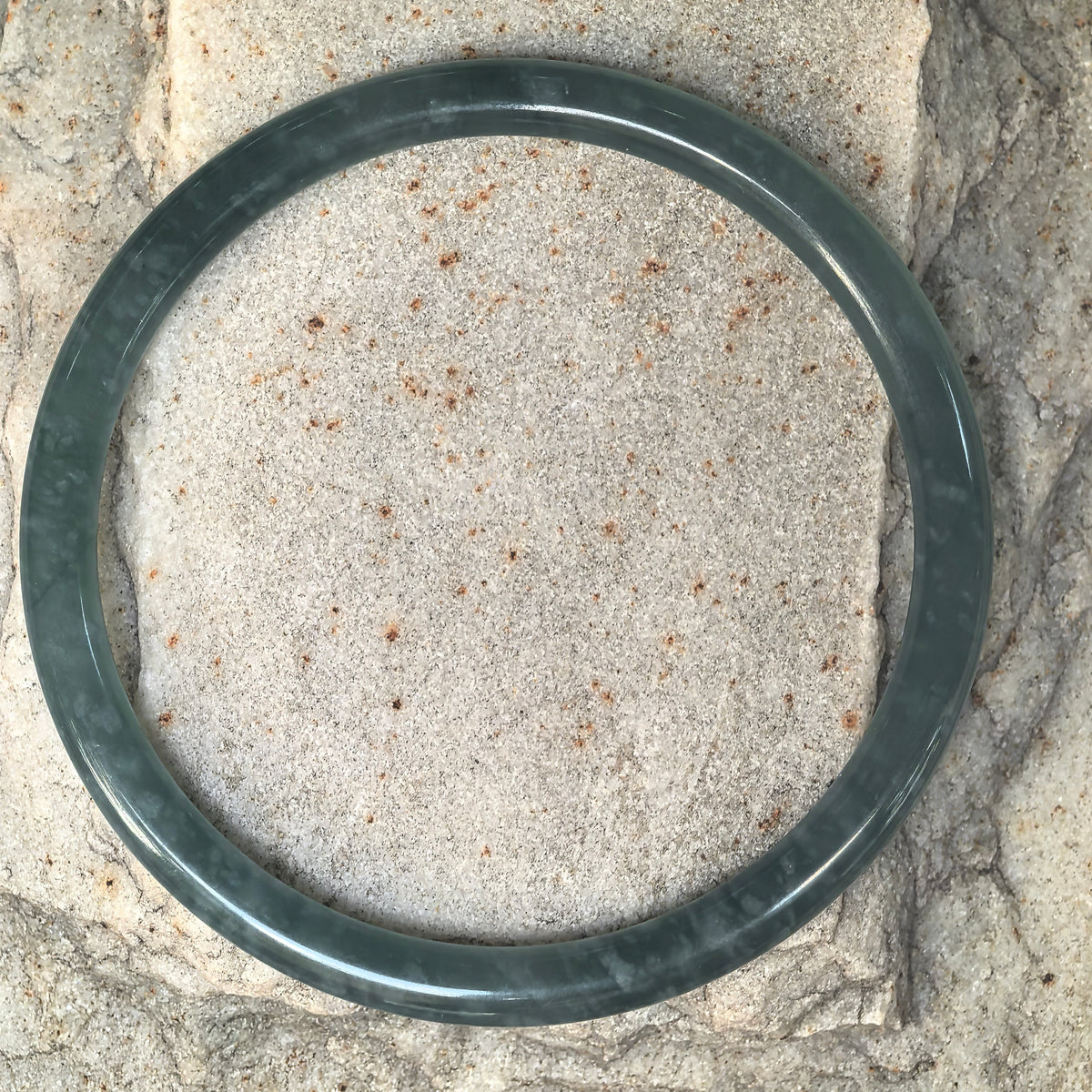 Top view of a green Guatemalan jadeite round-bar bangle on stone, showing its circular shape and cotton-like inclusions.
