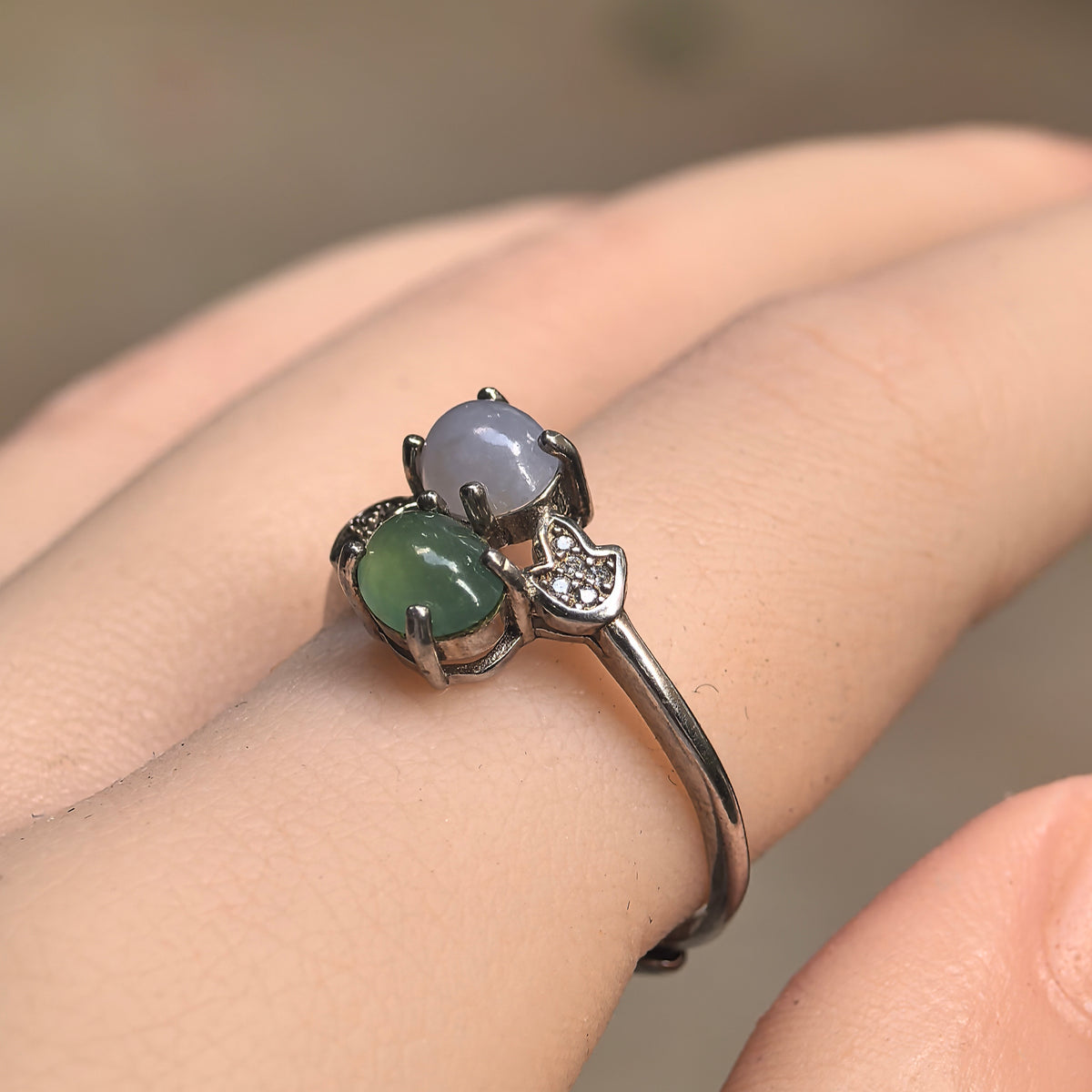 Angled view of a purple and green twin-stone jadeite ring worn on a finger, showing raised silver prong settings and clear accent stones.