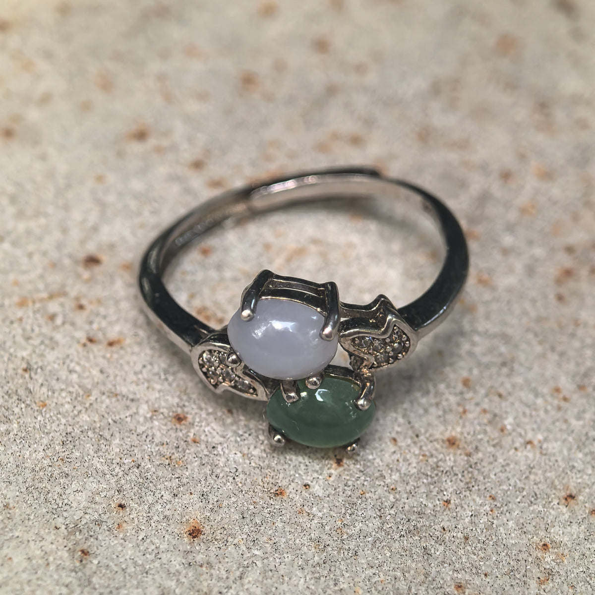 Close view of purple and green oval jadeite cabochons in silver prong settings, with clear accent stones on both shoulders.