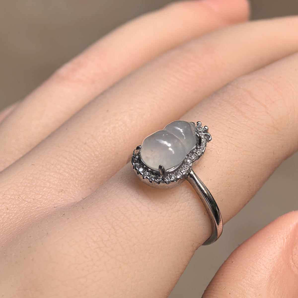 Angled view of a white jadeite gourd ring worn on a finger, showing the rounded carving, raised silver prong setting and clear stone halo.