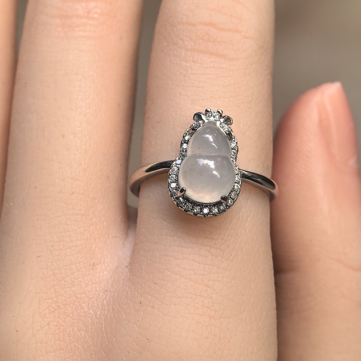 Front view of a white jadeite gourd ring on a textured stone surface, showing the clear accent stone halo and larger round accent at the top.