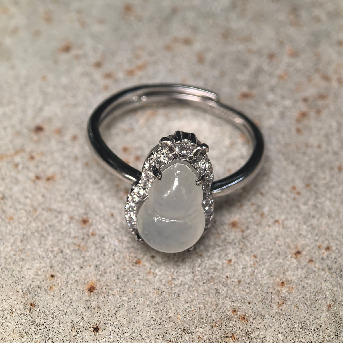Front view of a white jadeite gourd ring on a finger, with a contoured clear stone halo, curved silver details at the top and a smooth silver ring band.
