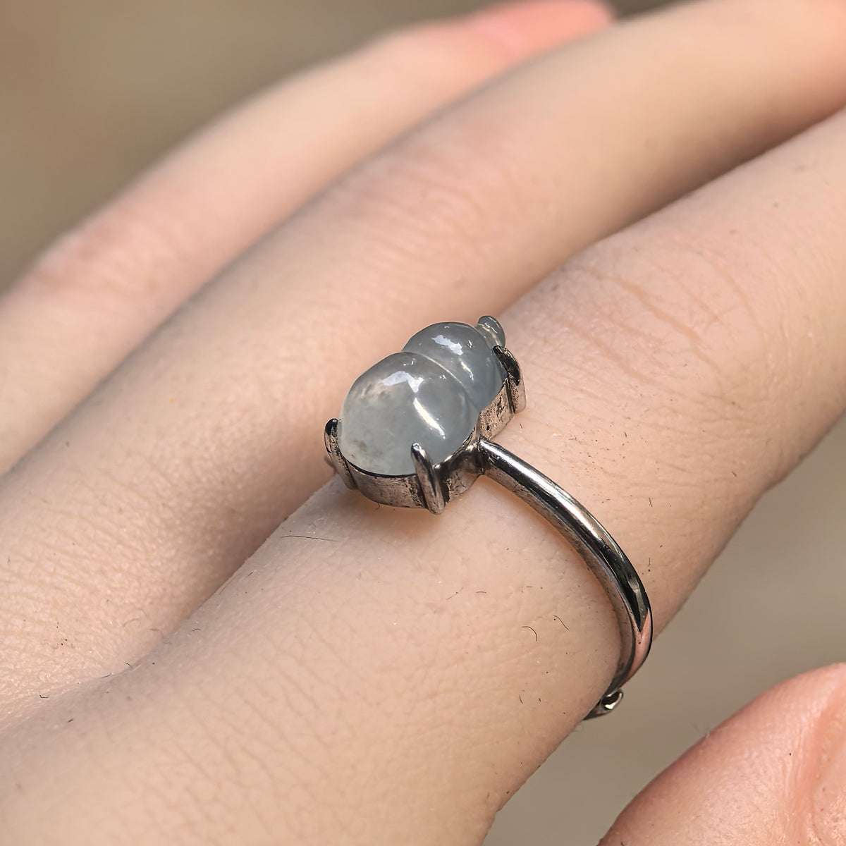 Angled view of a white jadeite gourd ring worn on a finger, showing the rounded carving, silver prongs and smooth S925 silver ring band.