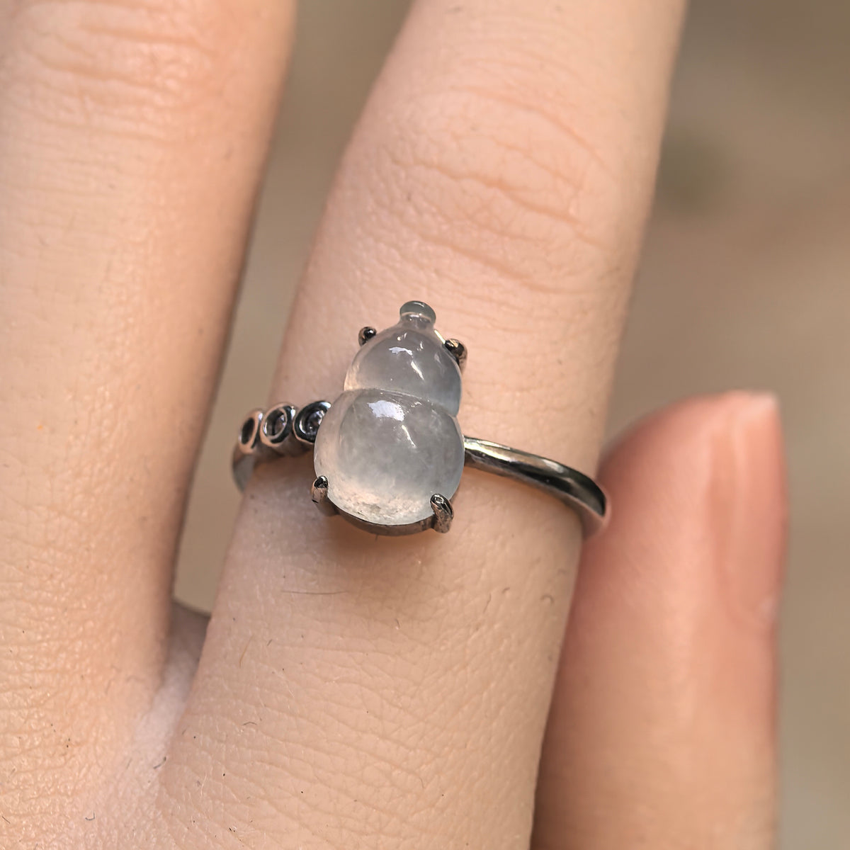 Front view of a white jadeite gourd ring on a finger, with round clear accent stones in circular silver settings on one side.