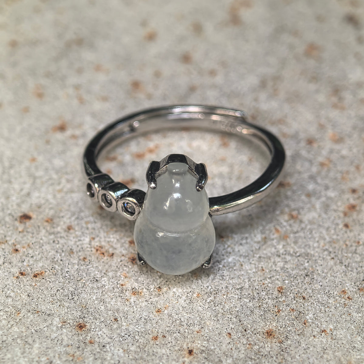 White jadeite gourd ring on a textured stone surface, showing the upright carving, visible cotton-like patches and row of round side accents.