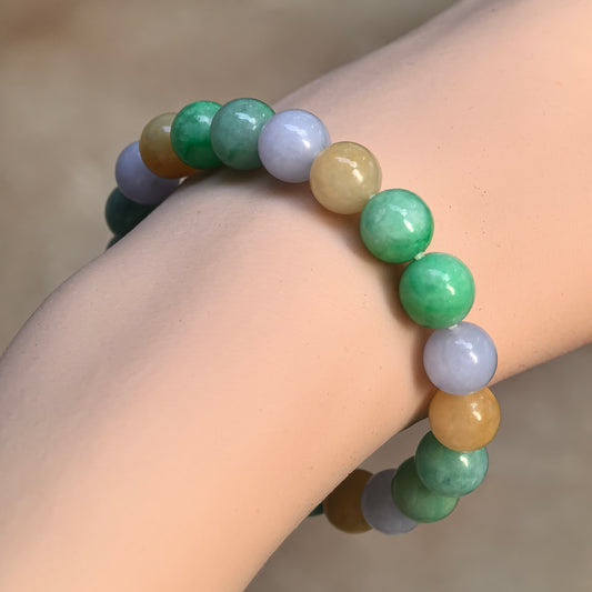 Angled wrist view of a glutinous multicolor jadeite bead bracelet showing mottled green beads alongside lavender and yellow tones.