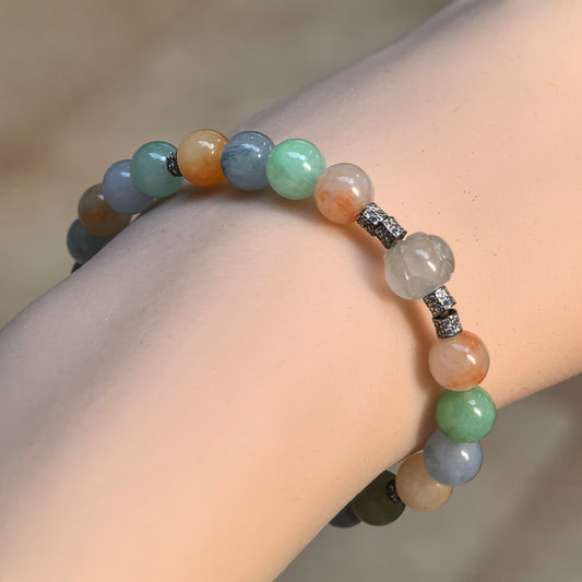 Angled wrist view of a multicolor jadeite bracelet with green, blue-gray and yellow round beads, a pale carved floral bead and silver-tone spacers.