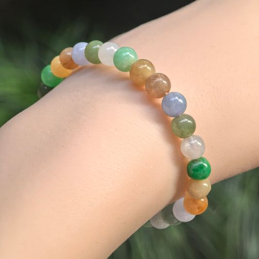 Angled wrist view of a multicolor jadeite bracelet with polished round beads in green, lavender, white, yellow and warm brown.
