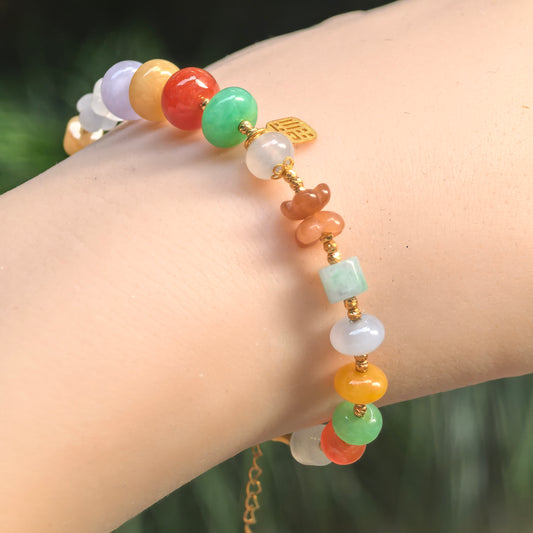 Angled wrist view of a multicolor jadeite bead bracelet with green, lavender, yellow and orange-red beads, carved accents and 18K gold spacers.