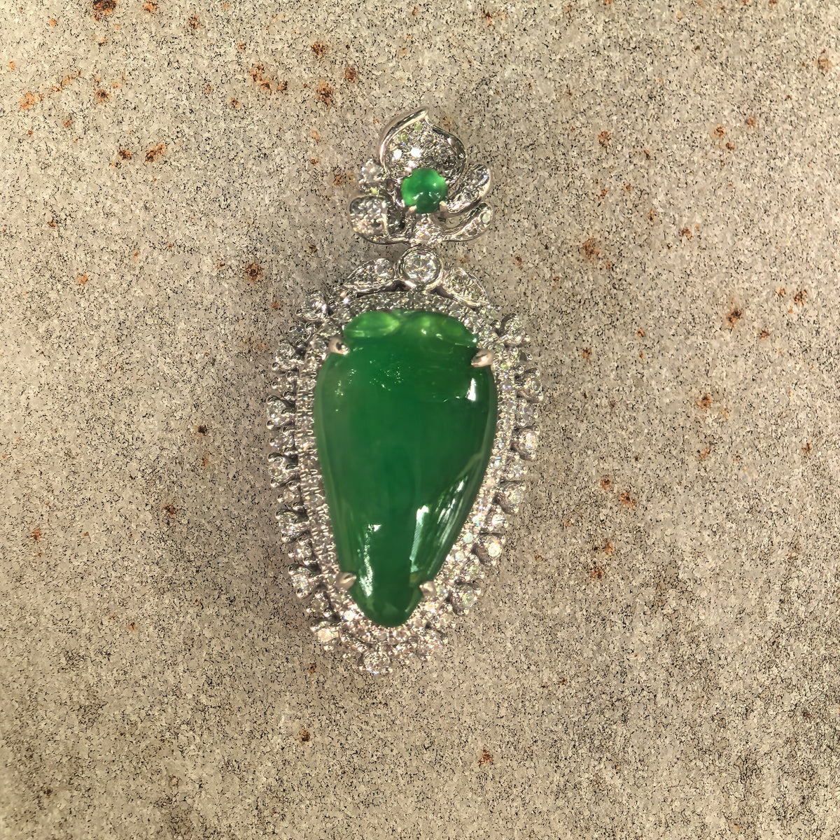 Green pear-shaped jadeite pendant displayed on its matching NGTC certificate against a woven background.