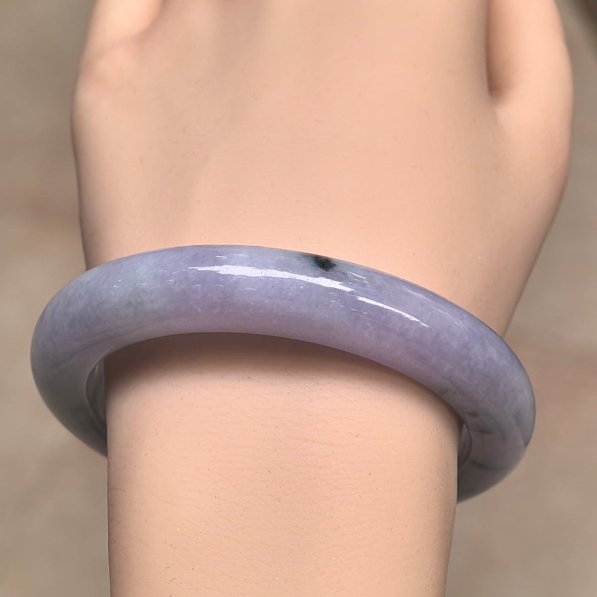 Front wrist view of a lavender jadeite bangle showing its rounded outer profile and a dark patch near the upper edge.