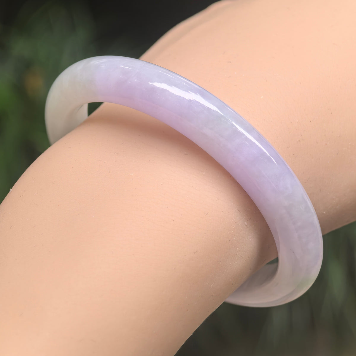 Angled wrist view of a pale lavender and light green jadeite bangle showing its polished rounded outer surface.