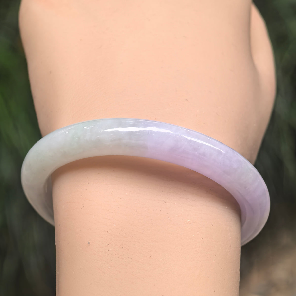 Front wrist view of a glutinous jadeite D-shape bangle with pale lavender and light green tones.