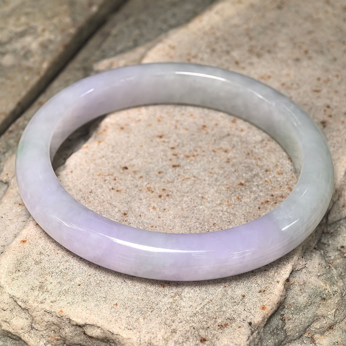 Angled view of a glutinous jadeite bangle on stone, showing pale lavender transitioning into light green.