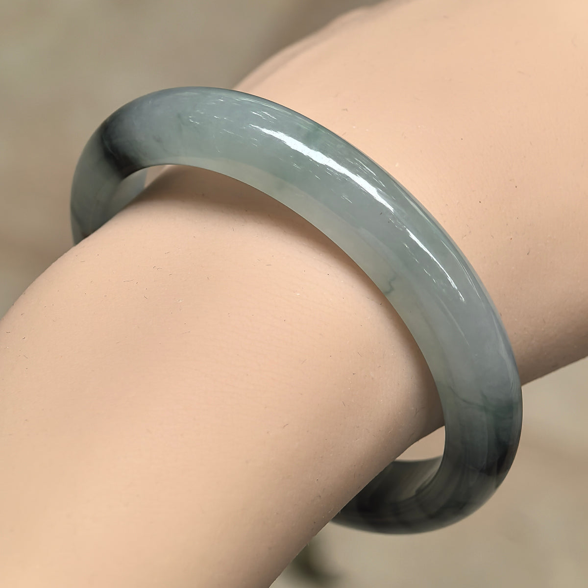 Angled wrist view of an icy glutinous light green D-shape jadeite bangle with concentrated dark floating patterns.