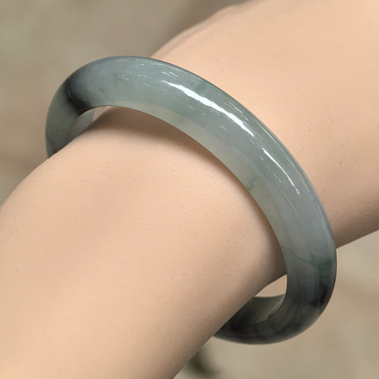Angled wrist view of an icy glutinous light green D-shape jadeite bangle with concentrated dark floating patterns.