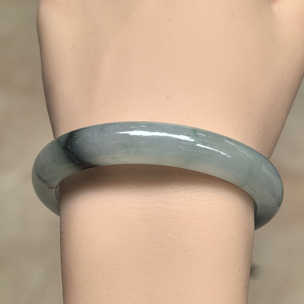 Front wrist view of a light green jadeite bangle showing its polished outer surface and contrasting dark patches.