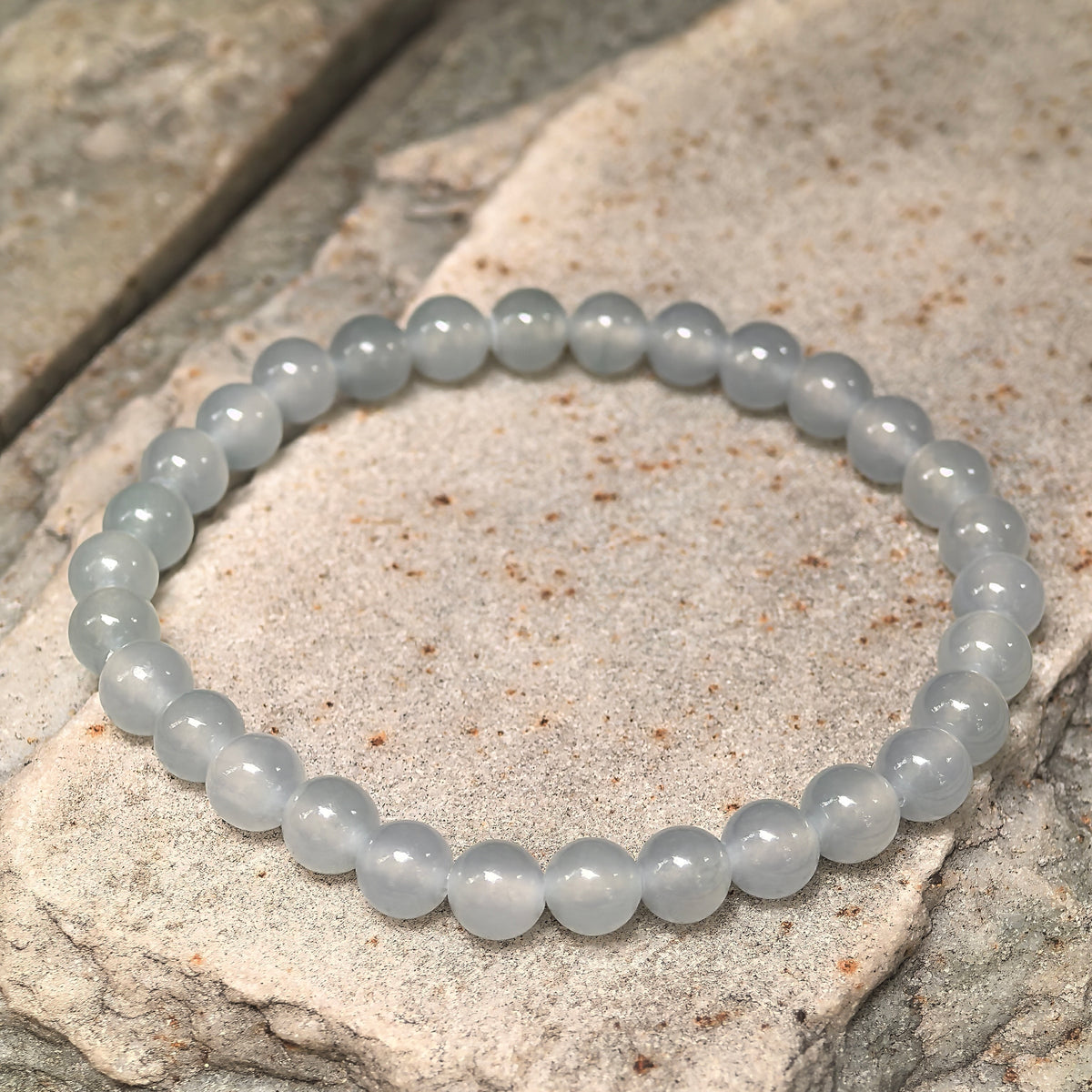 Angled view of a white round bead jadeite bracelet resting on a textured stone surface.