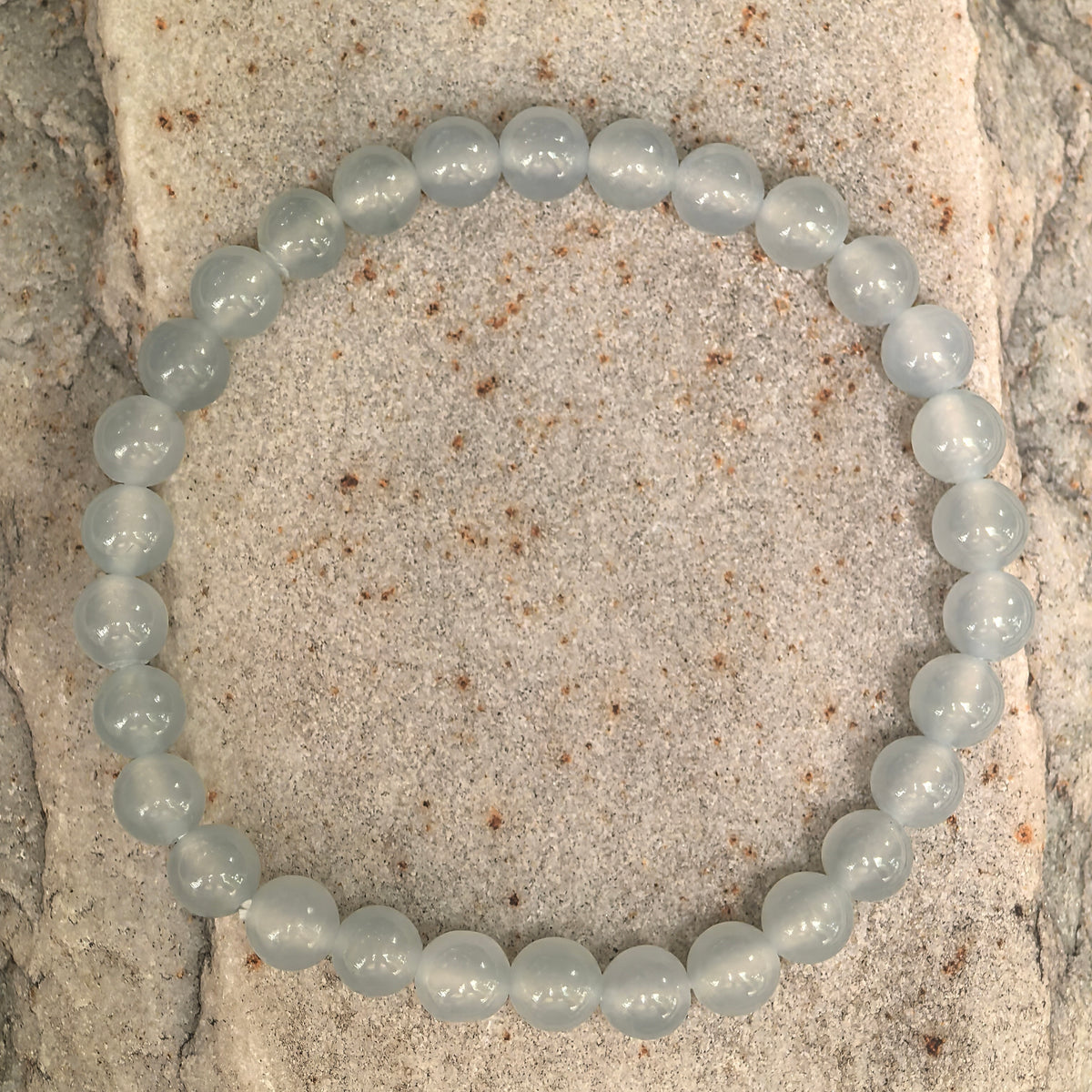 Close-up of icy white jadeite beads on stone, showing gel-like translucency, polished luster and internal textures.