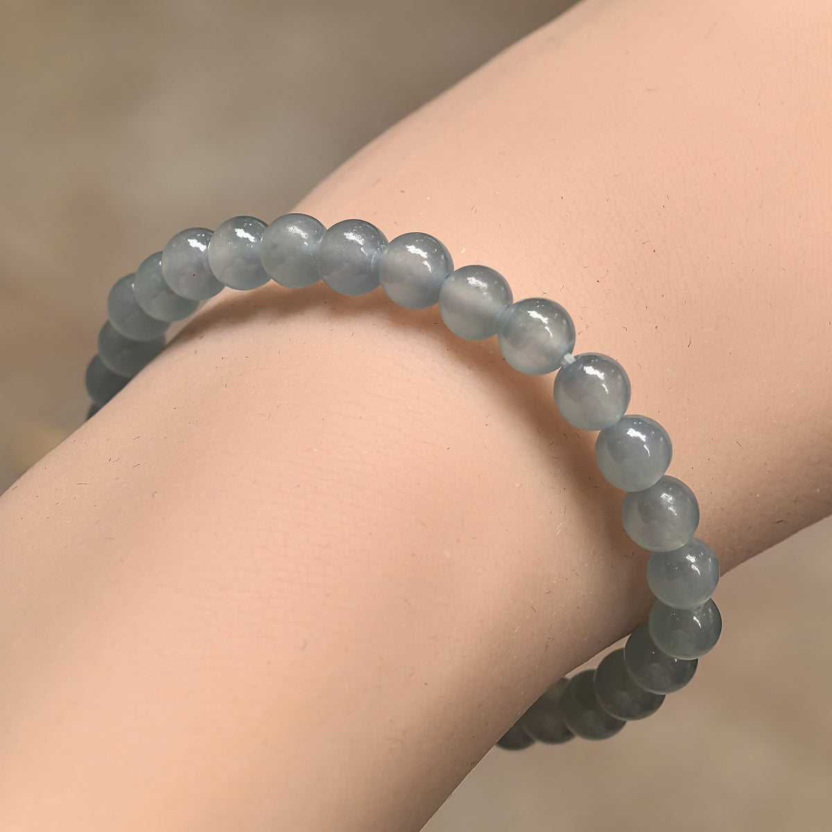 Angled wrist view of an icy light blue jadeite bracelet with polished round beads arranged in a slender single strand.