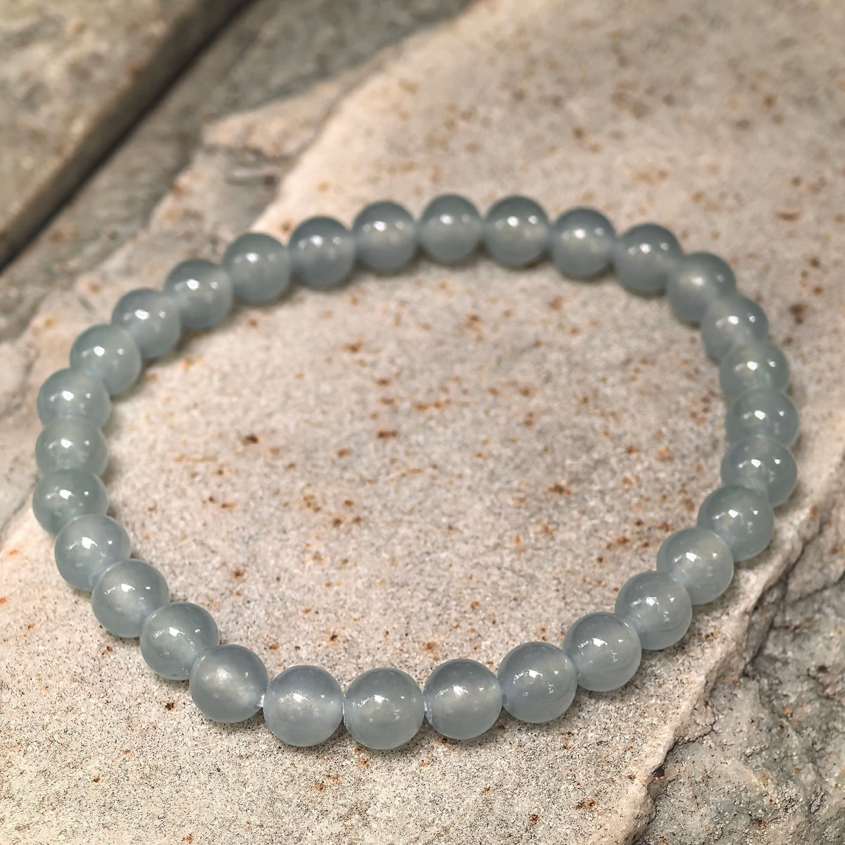 Angled view of an icy light blue round bead jadeite bracelet resting on a textured stone surface.