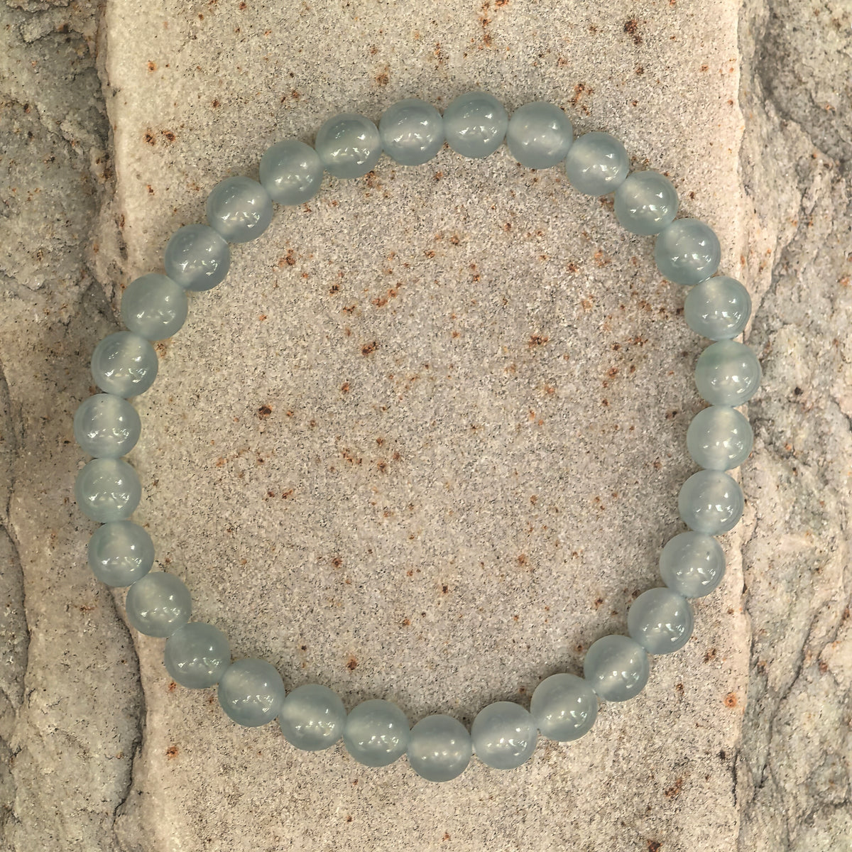 Overhead view of a light blue jadeite bracelet on stone, showing the complete strand of polished round beads.