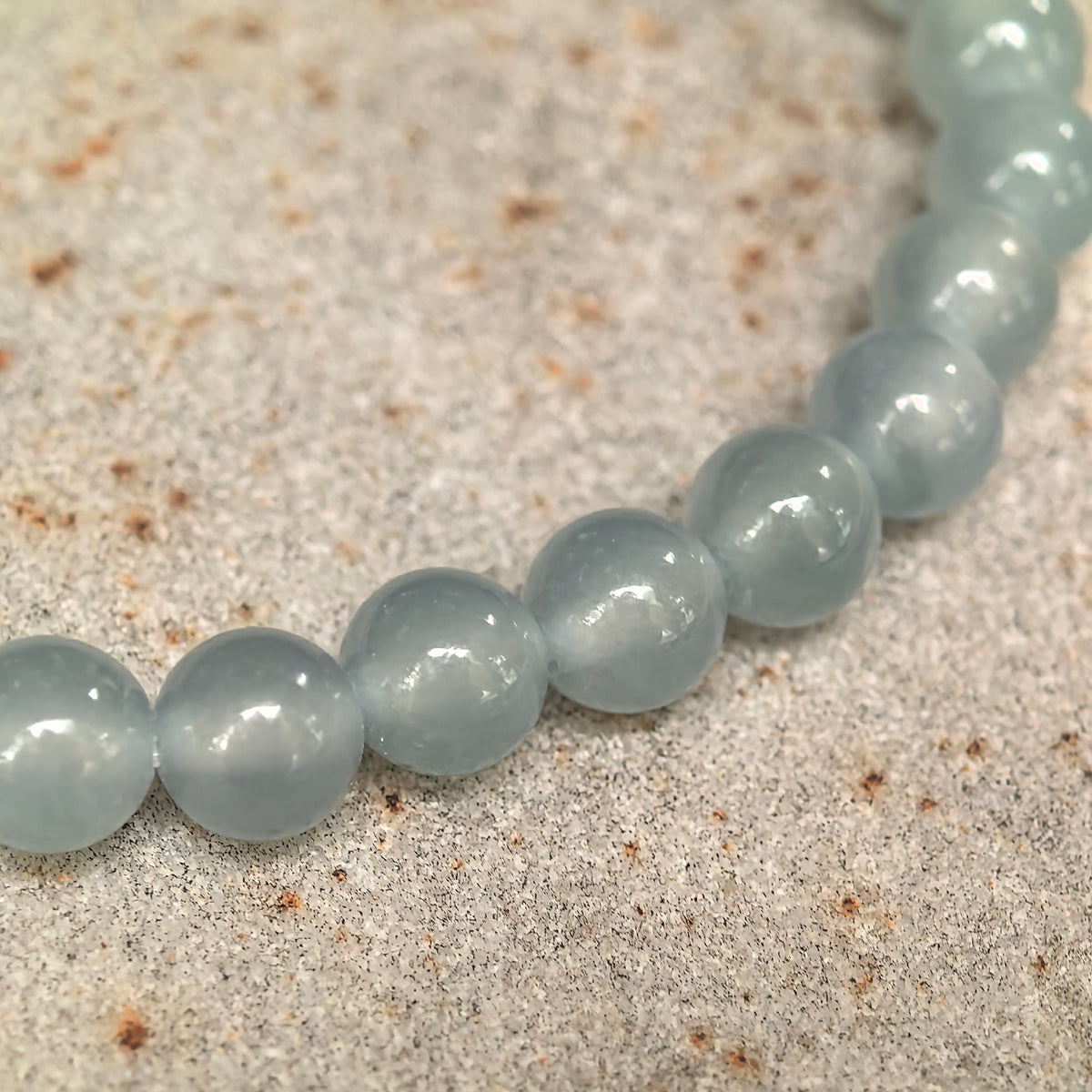Close-up of icy light blue jadeite beads on stone, showing their gel-like translucency, polished luster and internal textures.
