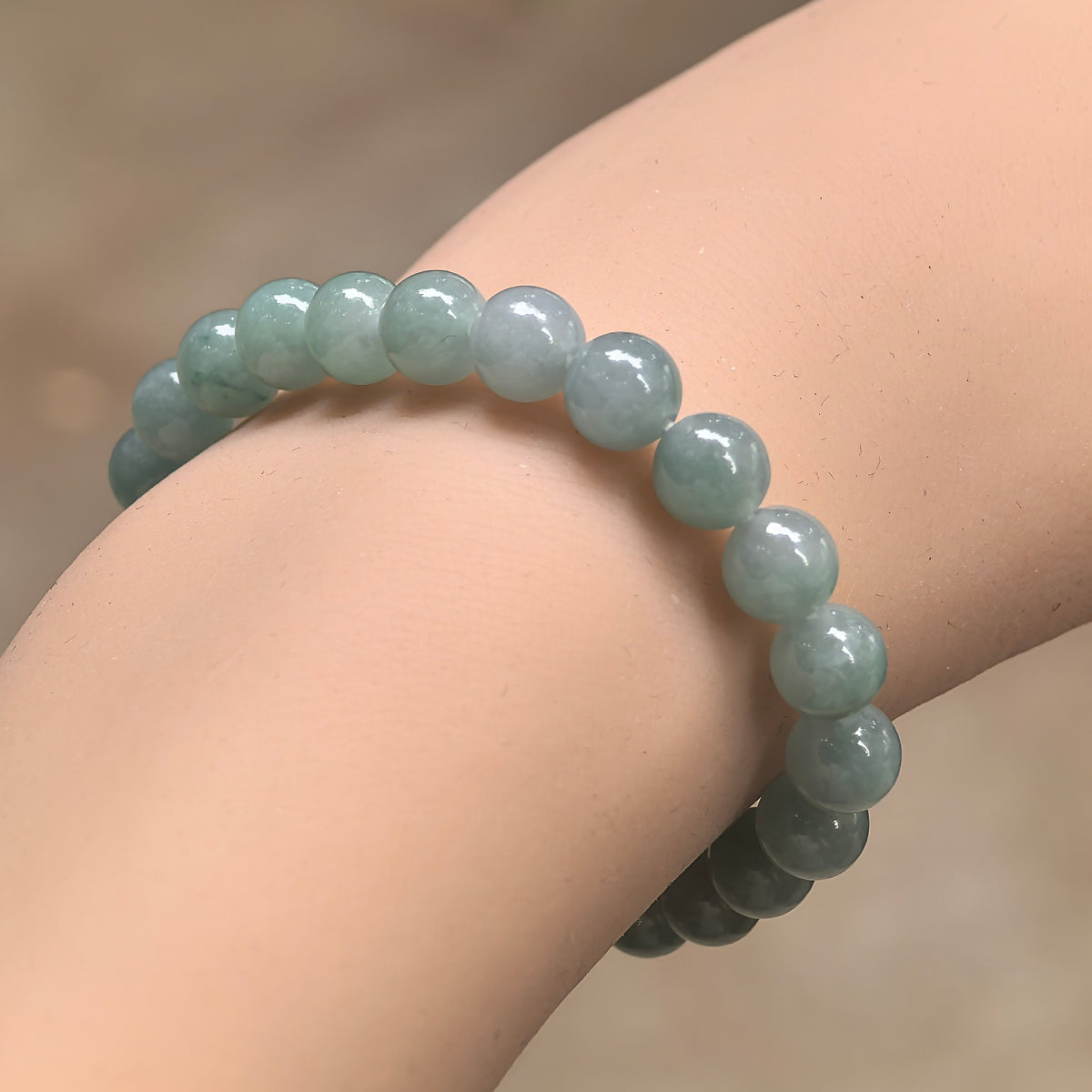 Angled wrist view of an icy glutinous light green jadeite bead bracelet arranged in a single strand.