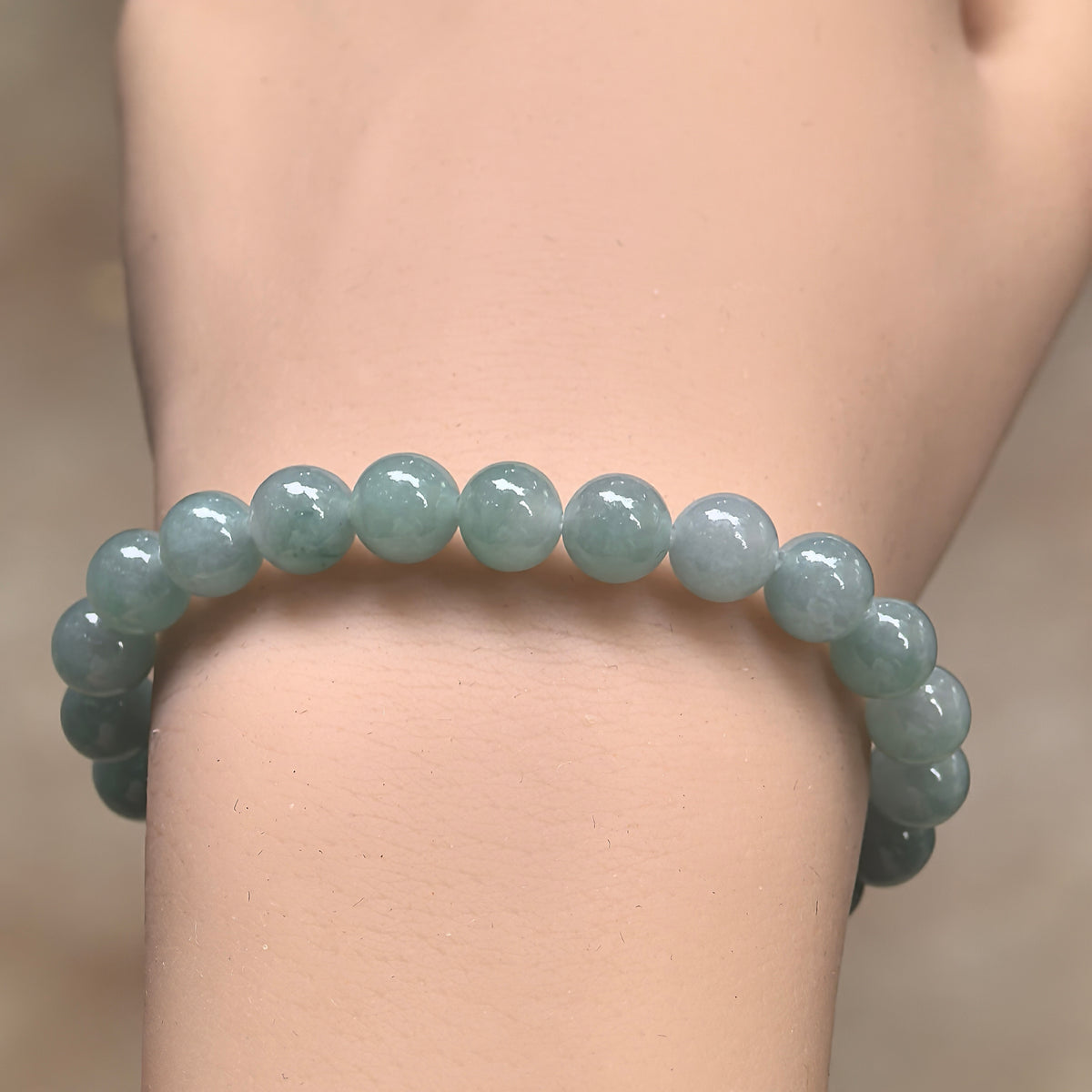 Front wrist view of a light green jadeite bracelet showing polished round beads and subtle variations in tone.