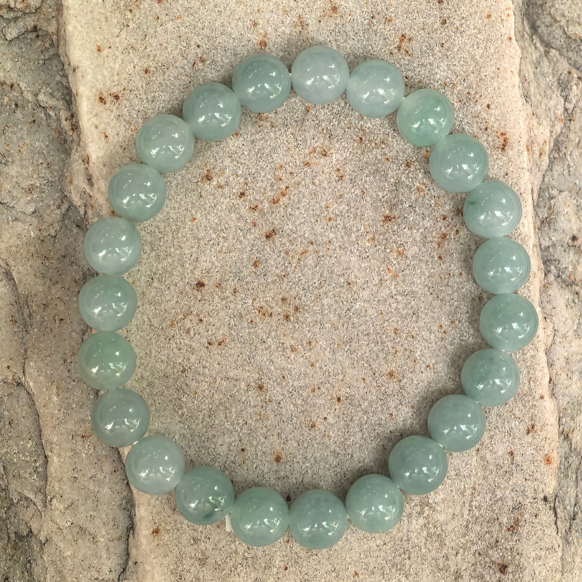 Overhead view of an icy glutinous light green jadeite bracelet on stone, showing the complete strand of round beads.