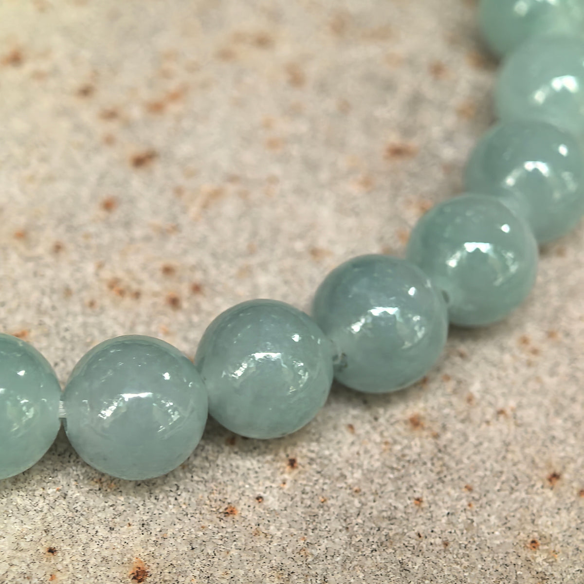 Close-up of light green round jadeite beads on stone, showing their polished luster and internal textures.