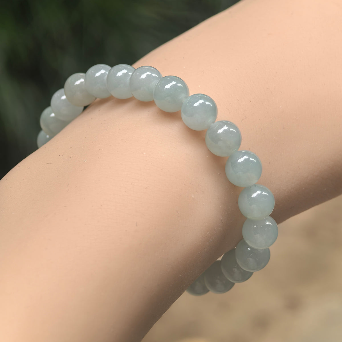 Angled wrist view of a pale green jadeite bracelet with polished round beads and soft translucency.