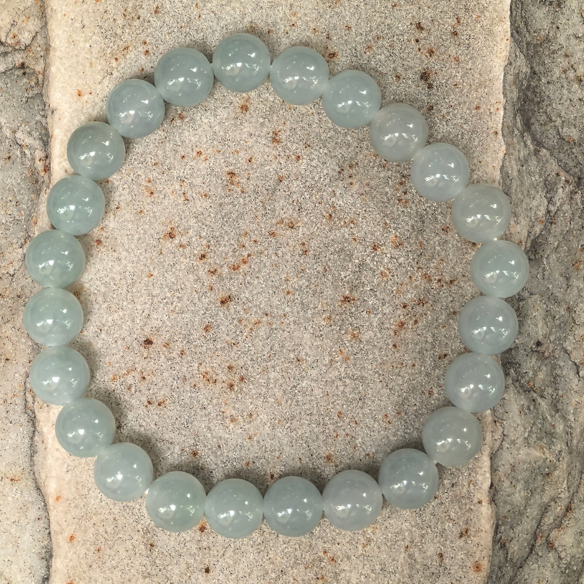 Overhead view of a pale green round bead jadeite bracelet on stone, showing the complete strand and gentle tonal variations.