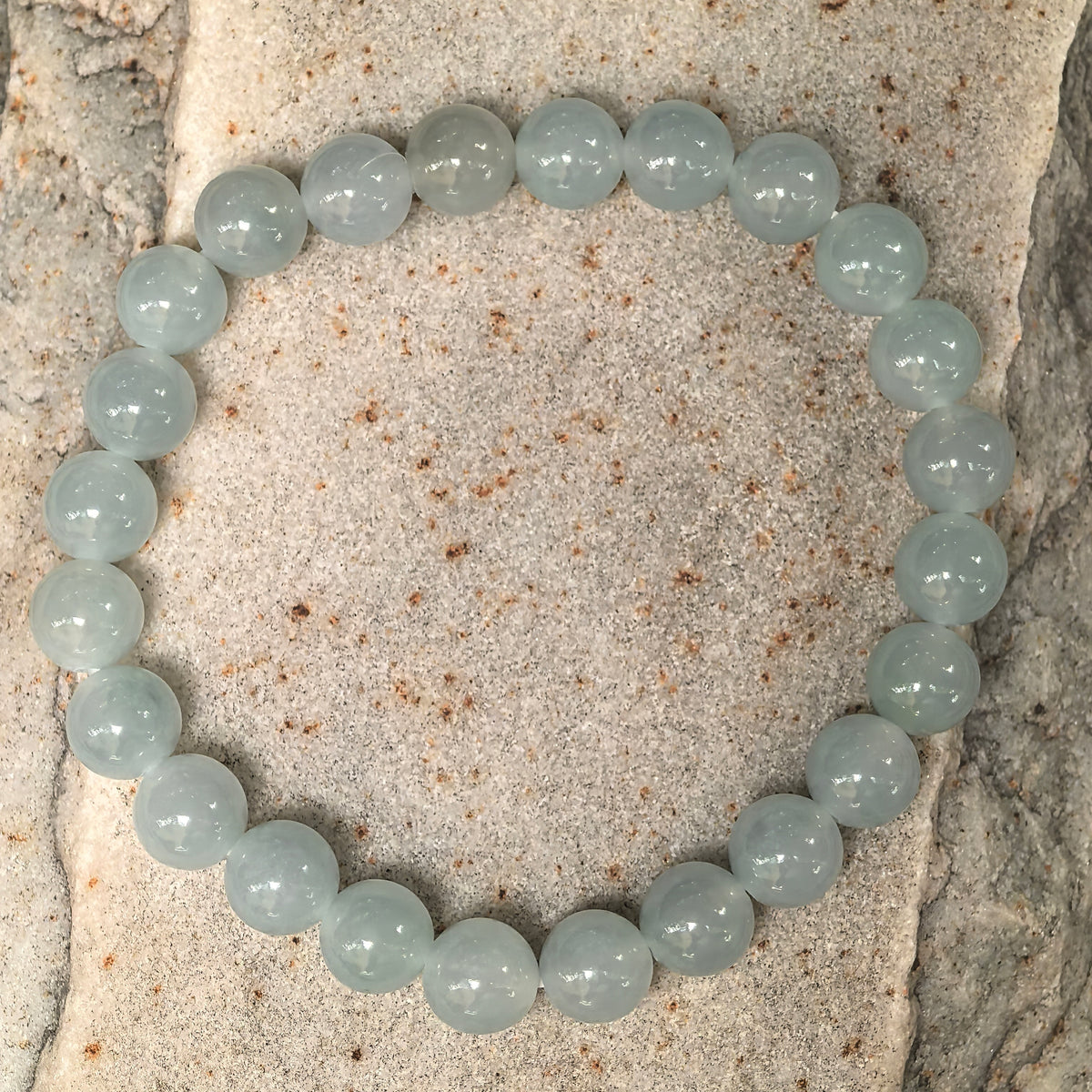 Close-up of pale green round jadeite beads on stone, showing their polished luster and internal textures.
