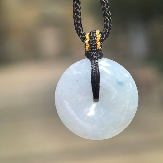Front view of a pale blue jadeite Peace Pendant suspended from a black knotted cord, showing its circular shape and polished surface.