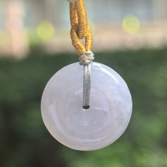 Front view of a pale lavender jadeite Peace Pendant suspended from a knotted cord, showing its circular shape and polished surface.
