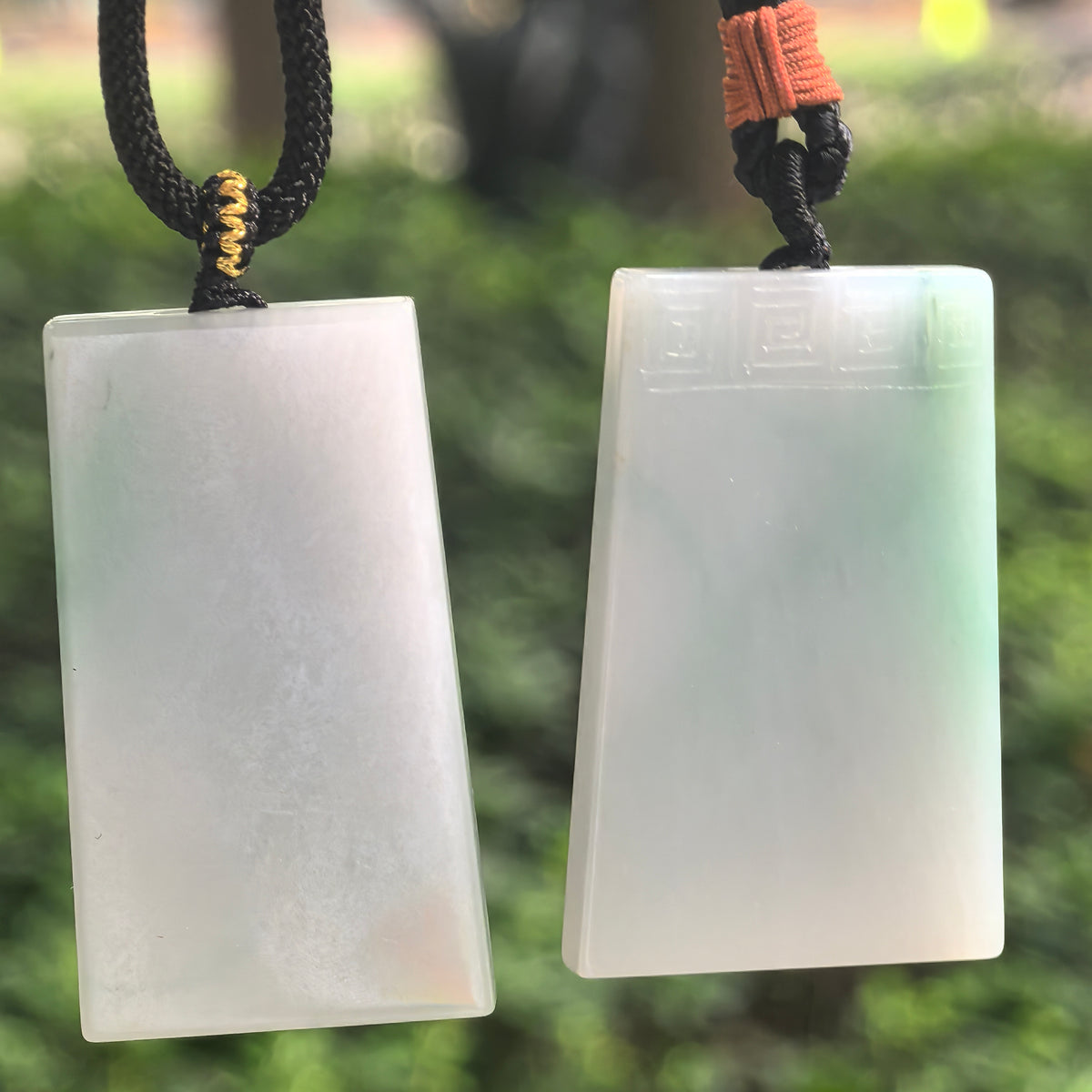 Two white jadeite Plain Plaque Pendants hanging side by side, with the uncarved style on the left and carved-border style on the right.