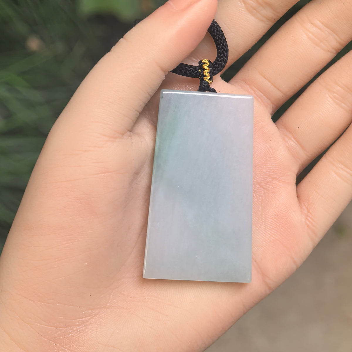 Uncarved white jadeite Plain Plaque Pendant resting in an open palm, showing its polished face and soft green accents.