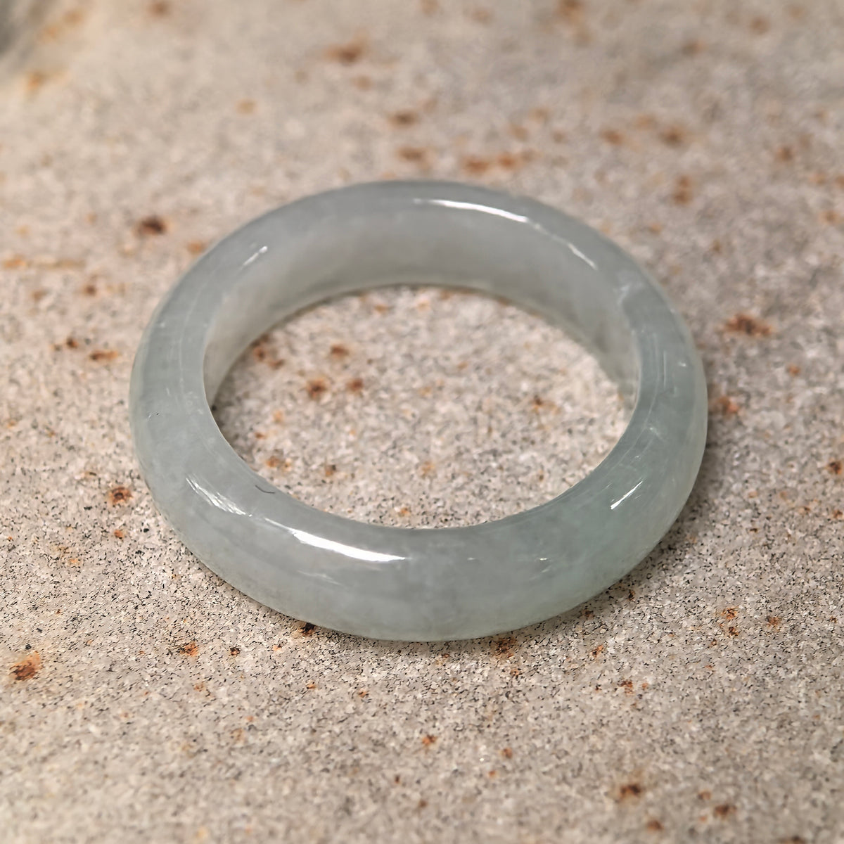 White jadeite ring band resting on stone at an angle, with its inner opening and gently rounded contours visible.