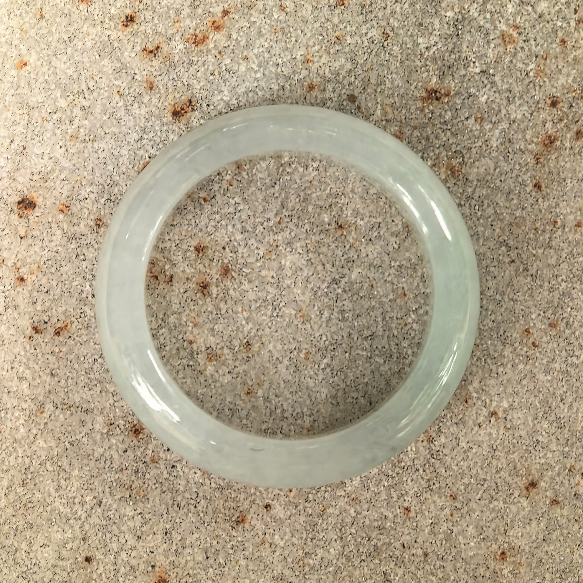 Overhead view of a white jadeite ring band on stone, showing its circular outline and natural texture.