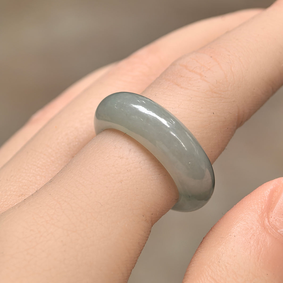 Angled view of a pale green jadeite ring band worn on a finger, showing its thick rounded profile and polished sheen.